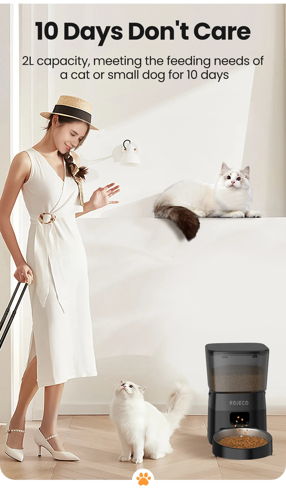 Woman in a white dress standing next to a pet feeder with two cats in a room.
